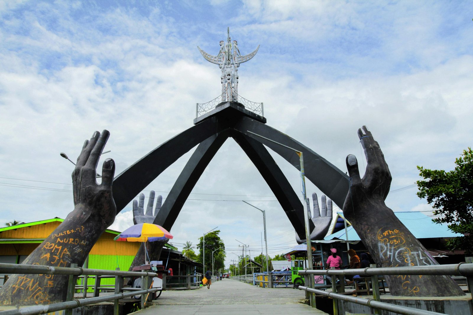 Monument in Agats, Papua with large hands sculpture and urban surroundings.